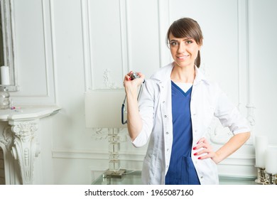 Happy Dark-haired Nurse Wearing White And Blue Medical Scrubs Is Standing With Phonendoscope In Her Hand