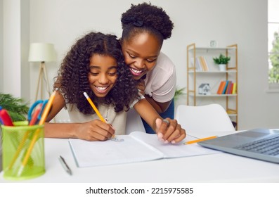 Happy dark-skinned mother watching her cheerful teenage daughter write and draw at home. Woman hugs her daughter who is studying and doing creativity while sitting in front of laptop. Family concept. - Powered by Shutterstock