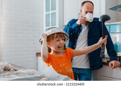 Happy Daughter And Father Playing In Kitchen In Morning. Child Kid Girl Put Colander Bowl On Her Head With Ladle In Hand She Have Fun And Laughs Plays Game. Happy Time Together Family In Cooking Time