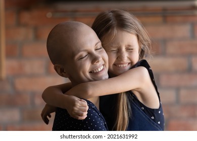 Happy Daughter Girl Hugging Mom With Cancer, Holding Tight, Smiling With Closed Eyes. Little Kid Giving Love, Motivation To Ill Hairless Young Mother During Chemotherapy. Family Support Concept