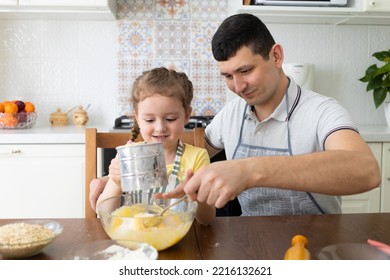 happy daughter help to father in kitchen. kid cooking food with dad. little girl, man in apron in preparing dough. child baking pie, playing with flour. family together home - Powered by Shutterstock