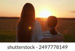 Happy daughter hugs mother outdoors. Child, girl hugging her mother in summer park in sun. Happy family on walk in field looking to future. Mom, child hugs together on sunny day. Carefree childhood