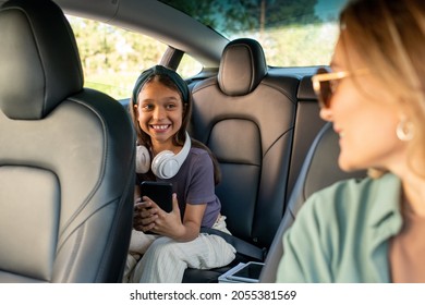 Happy Daughter Looking At Her Mom While Sitting On Backseat Inside Electric Car