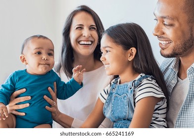 Happy daughter sitting on father legs and looking his little brother. Excited infant playing with elder sister. Portrait of smiling multiethnic family sit on sfoa and enjoying at home.