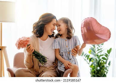 Happy Day! Child Daughter Is Congratulating Mother And Giving Her Flowers. Mum And Girl Smiling And Hugging. Family Holiday And Togetherness.