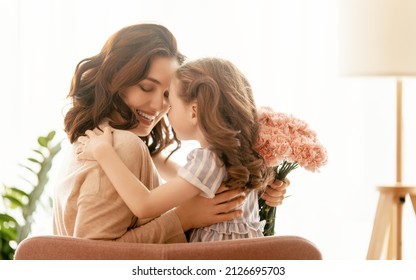 Happy day! Child daughter is congratulating mother and giving her flowers. Mum and girl smiling and hugging. Family holiday and togetherness. - Powered by Shutterstock