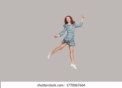 Happy delicate girl in vintage ruffle dress levitating with ballet dance move, hovering in mid-air and smiling joyfully, jumping trampoline, flying up. indoor studio shot isolated on gray background