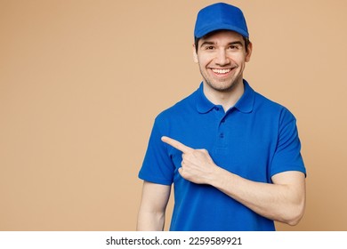 Happy delivery guy employee man wearing blue cap t-shirt uniform workwear work as dealer courier pointing index finger aside indicate on area isolated on plain light beige background. Service concept - Shutterstock ID 2259589921