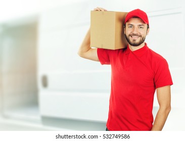 happy delivery man with box on shoulder in front of a truck