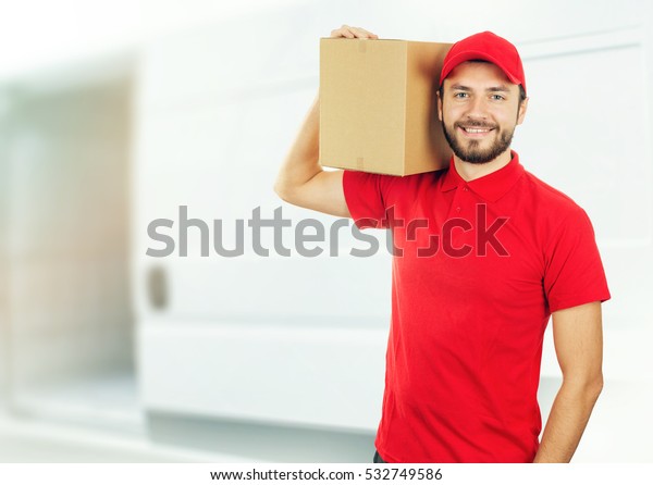happy delivery man with box on shoulder in front of\
a truck