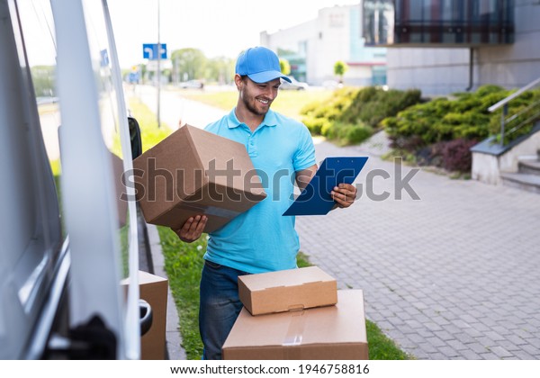 Happy delivery man with a lot of cardboard boxes\
near his van on a city\
street