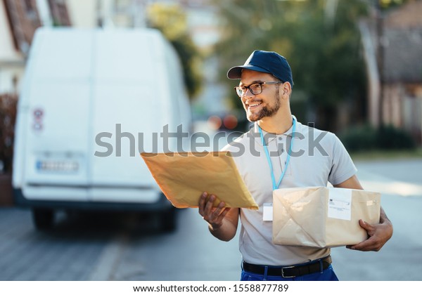 Happy delivery man carrying packages while walking down\
the street. 