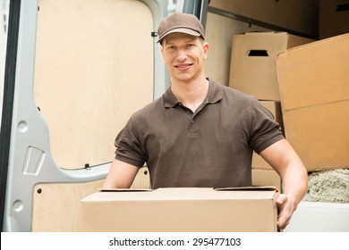 Happy Delivery Man Holding Box In Front Van