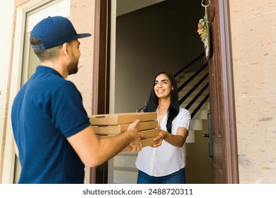 Happy delivery man holding cardboard pizza boxes while delivering food order to a woman at the front door - Powered by Shutterstock