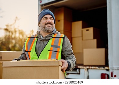 Happy delivery man loading cardboard boxes into a truck and looking away.  - Powered by Shutterstock