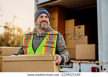 Happy delivery man loading cardboard boxes into a truck and looking away. 