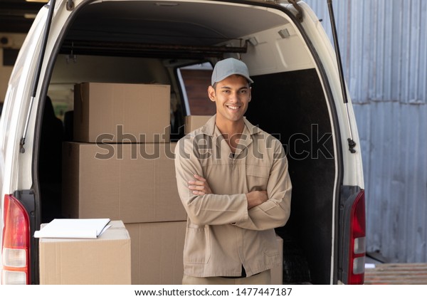 Happy delivery man standing with arms crossed\
near van outside the warehouse. This is a freight transportation\
and distribution warehouse. Industrial and industrial workers\
concept