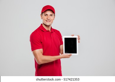 Happy Delivery Man With Tablet In Studio. Isolated Gray Background