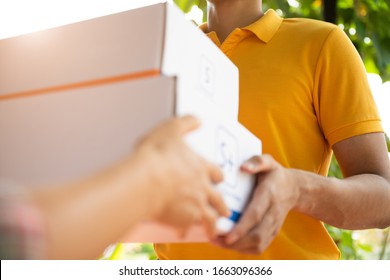 Happy Delivery Man In Yellow Polo Shirt Uniform With Parcel Post Box In Hands Standing In Front Of Customer's House Doors. Smiling Courier Delivery Man.