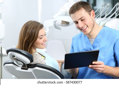 Happy Dentist And Patient Commenting Treatments In A Tablet Application In A Consultation With Medical Equipment In The Background