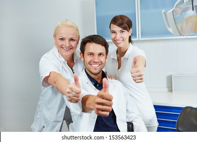 Happy dentist and smiling dental team holding their thumbs up in dental practice