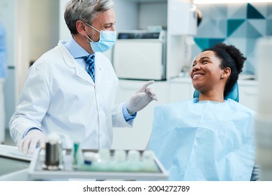 Happy Dentist Talking To Black Female Patient During Dental Exam At Dentist's Office.