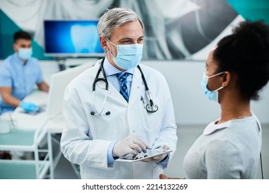 Happy Dentist Using Touchpad While Communicating With African American Woman At Dental Clinic.