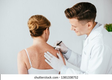 Happy Dermatologist In Latex Gloves Holding Marker Pen Near Woman With Melanoma Isolated On White 