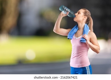 Happy Determined Athlete, Beautiful Woman Stands On A City And Drinks Water, Resting After Early Morning Jog At Sunrise