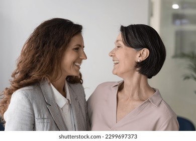 Happy different age women colleagues, workmates laughing hugging standing at workplace, enjoy business success and promotion, having friendly work relations. Friendship, family bond and relationships - Powered by Shutterstock