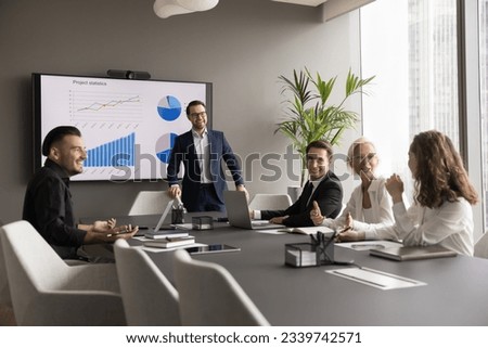 Happy different aged business team having fun on office meeting, talking, laughing, brainstorming at conference table. Positive confident male speaker, presenter giving statistic report to group