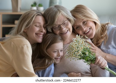 Happy different female generations family portrait. Grandkid woman, mature daughter, pretty cute girl kid hugging cheerful elderly grandma, holding flowers, celebrating mothers day - Powered by Shutterstock