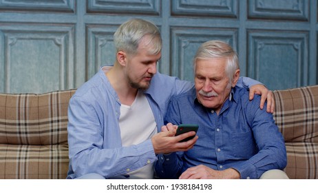 Happy Different Male Generations Family Senior Father And Son Watching On Online Mobile Phone Internet With Fun, Elderly And Young Man Leisure At Home Relax Together, Resting, Communication, Lifestyle