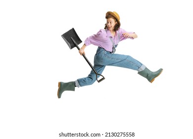 Happy Digger. Dynamic Portrait Of Young Girl, Female Gardener In Work Uniform And Gumboots Running Away Isolated On White Background. Concept Of Emotions, Agronomy. Funny Meme Emotions. Copy Space For