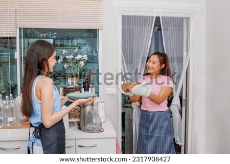 Happy dinner at home : Cheerful asian woman walks out of the kitchen wearing thermal gloves serving warm appetizing food from the microwave, have a female friend put a plate and pick it up from hand.