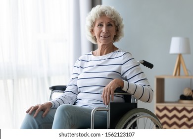 Happy disabled elder grandma patient sit on wheelchair alone at home hospital, smiling old woman on wheel chair look at camera in retirement house, seniors disability handicap healthcare concept