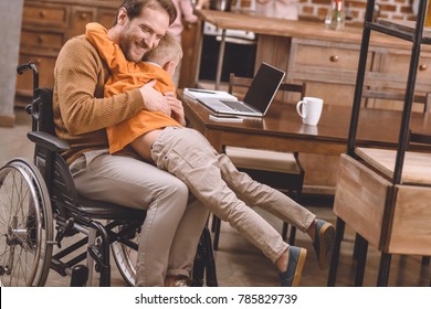 happy disabled father in wheelchair hugging with cute little son at home