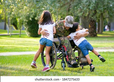 Happy Disabled Military Man In Wheelchair Returning Home And Hugging Kids. Veteran Of War Or Family Reunion Concept