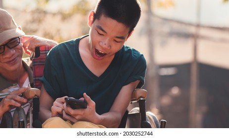 Happy disabled teenage boy on wheelchair and father selfie by mobile phone in outdoors background, Caring for handicapped kid for good mental health and diverse family concept.