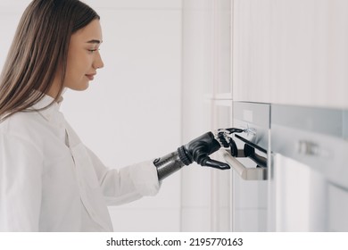 Happy Disabled Woman With Robotic Cyber Hand Is Switching Oven On. Amputee Is Cooking At Home Using Bionic Limb. Software In Fingers And Wrist Joint. Innovation And Orthopedic Technologies.