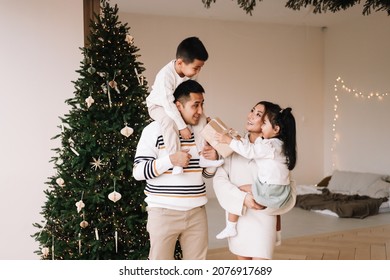 A Happy Diverse Asian Family Celebrates Christmas. Parents With Children Give Gift Boxes Decorate The Christmas Tree And Prepare For The New Year Holiday In A Decorated House. Selective Focus