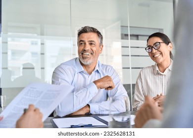 Happy diverse business people international corporate executive team talking at group meeting. Smiling older Latin male manager working with colleagues collaborating at boardroom table. - Powered by Shutterstock