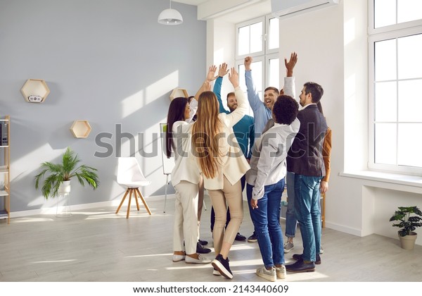 Happy diverse business team celebrating success\
and having fun all together. Group of cheerful ecstatic people\
standing in circle in modern office high five each other and shout\
Yes we did it, Hooray
