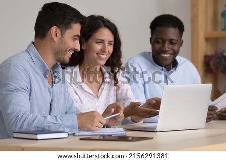 Happy diverse business team sharing laptop computer, watching online project presentation together, making video call. Coach training new group of interns for job tasks, showing work software