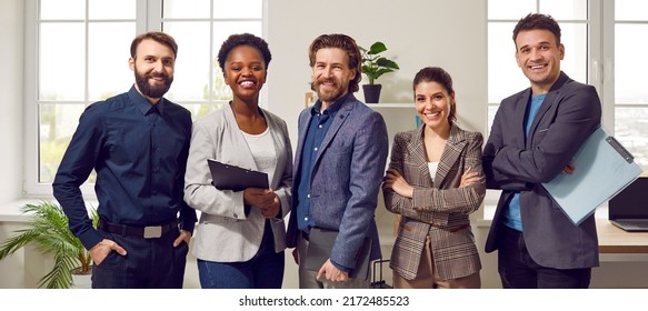 Happy Diverse Business Team Standing In The Office. Five Cheerful Confident Successful People In Smart Casual Suits Smiling And Posing For A Group Photo All Together. Banner. Work And Success Concept