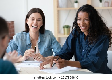 Happy Diverse Colleagues Employees Having Fun At Meeting, Sitting At Table Together, Business Partners Discussing Project, Sharing Ideas, Laughing At Joke, Engaged In Team Building Activity