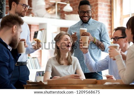 Happy diverse colleagues have fun at lunch break in office, smiling multiracial employees laugh and talk eating pizza and drinking coffee, excited workers celebrate shared win ordering takeaway food