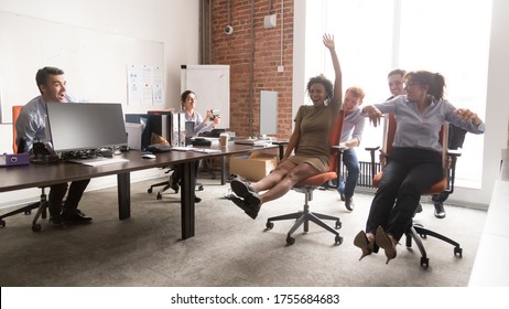 Happy Diverse Colleagues Having Fun Together, Riding In Office Chair, Excited Employees Laughing, Enjoying Funny Game During Break, Celebrating Friday, Team Building Activity, Horizontal Photo