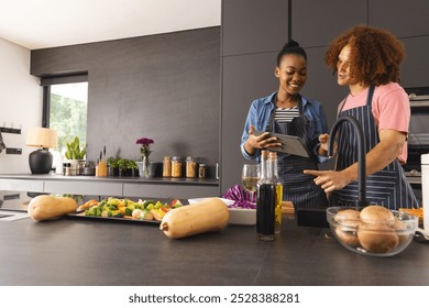 Happy diverse couple in aprons preparing meal, using tablet in kitchen, copy space. Food, cooking, togetherness, relationship, communication, recipe, lifestyle and domestic life, unaltered. - Powered by Shutterstock