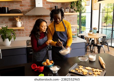 Happy diverse couple baking christmas cookies mixing dough in sunny kitchen, copy space. Cooking, baking, food, christmas, celebration, tradition, togetherness, domestic life and lifestyle, unaltered. - Powered by Shutterstock